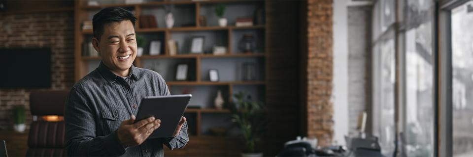 A confident Singaporean entrepreneur smiles while using a tablet in an office. The image reflects Green Card opportunities in the U.S. through the EB5 investment visa.