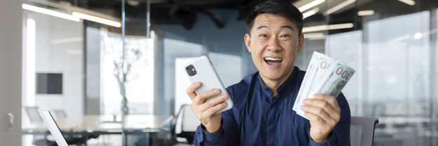 Happy EB5 investor holding smartphone and hundred-dollar bills after receiving capital repayment from a successful regional center project.