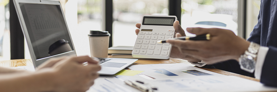 Two professionals reviewing EB5 investment returns and financial projections using a calculator, laptop, and printed charts during due diligence.