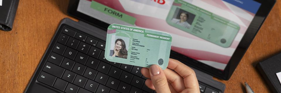 Close-up of a U.S. permanent resident card held in hand with a digital USCIS form in the background, representing the EB5 Green Card application process.