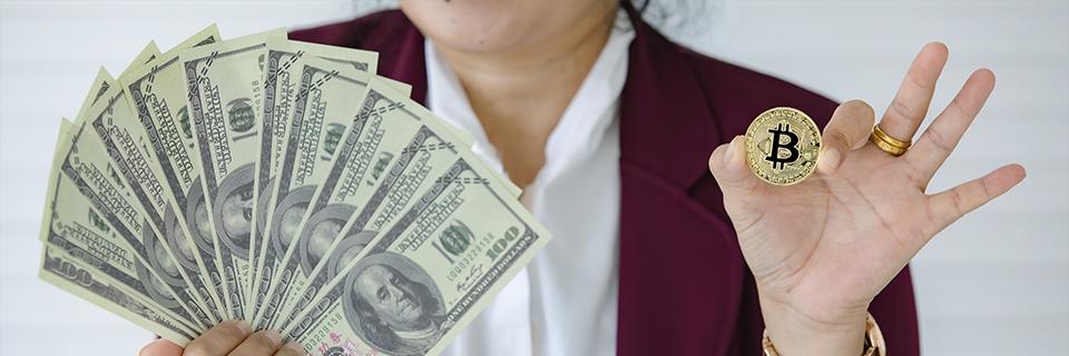 Investor displaying a physical Bitcoin and a fan of U.S. hundred-dollar bills, illustrating the conversion of crypto to fiat for use in the EB5 investment process.