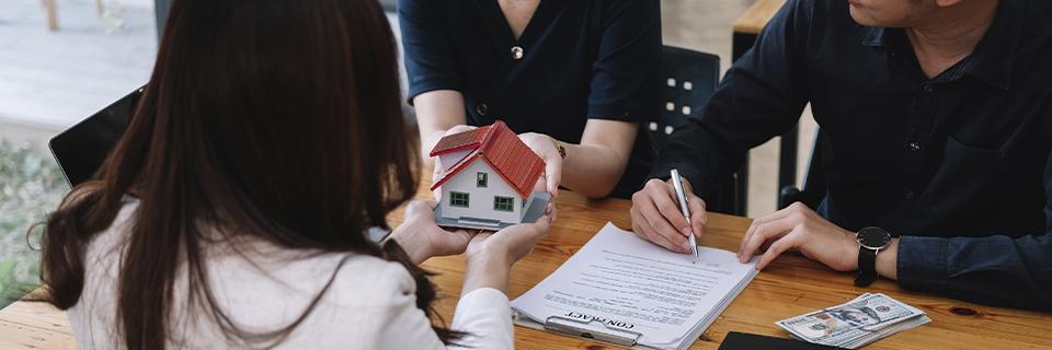 A couple sitting at a table with a loan officer, reviewing mortgage documents for a home—as a step in establishing source of funds for an EB5 investment.