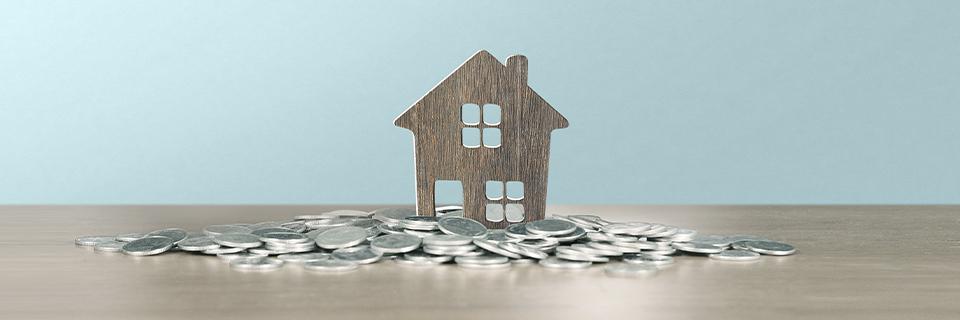A small wooden house model surrounded by silver coins symbolizing home equity value—often used to fund EB5 investments via a HELOC.