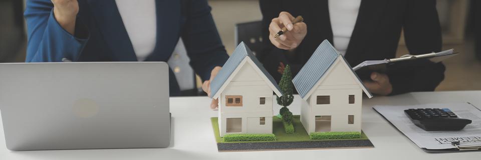 Two regional center industry professionals analyzing model houses and documents during a financial consultation, illustrating the planning involved in using home equity for EB5 visa funding.