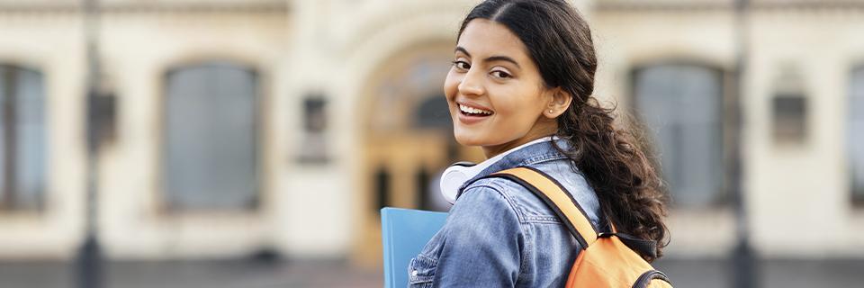 A smiling international student with a backpack and books standing outside a U.S. university, representing OPT students exploring EB5 visa options.