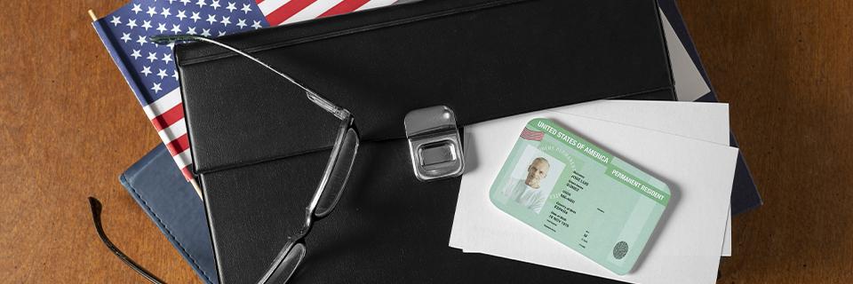 Close-up of a U.S. Green Card on a desk with American flag folder, paperwork, and reading glasses—representing lawful permanent residency and immigrant visa documentation process.