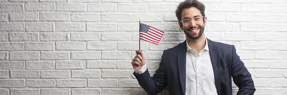 Confident man holding U.S. flag while smiling at camera, representing success, permanent residency, and embracing U.S. citizenship through EB5 investment.