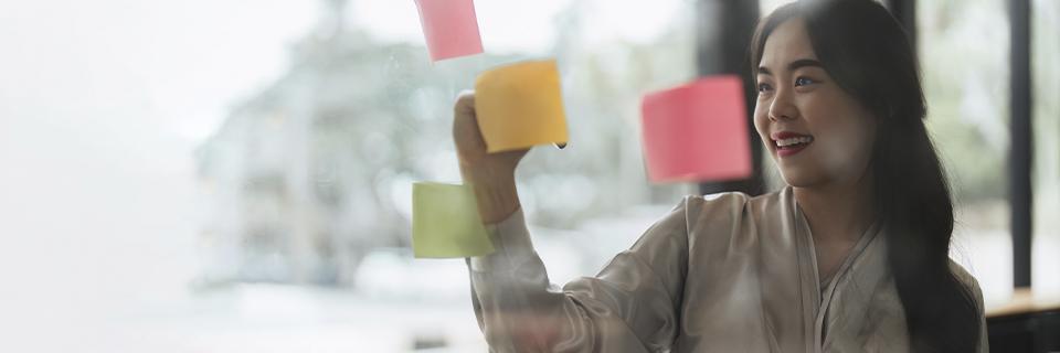 Smiling woman placing sticky notes on glass, representing education planning, career flexibility, and new opportunities through EB5 visa residency.