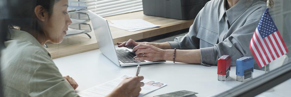 EB5 visa applicant at a U.S. immigration office desk, preparing documents and discussing permanent residency application with an officer.