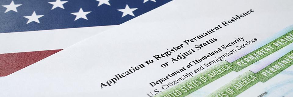 Close-up of Form I-485 with a partial view of a U.S. permanent resident card and flag, representing adjustment of status through the EB5 program.