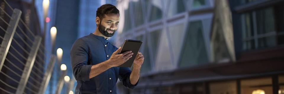 Young Indian professional checking updates on a tablet in a city business district, representing the career flexibility and stability offered through the EB5 Green Card program.