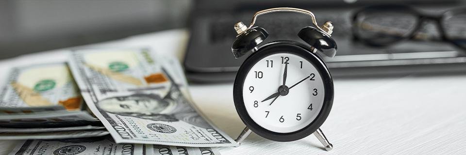 A classic black alarm clock rests beside hundred-dollar bills, illustrating the critical link between time and capital in EB5 visa investments.