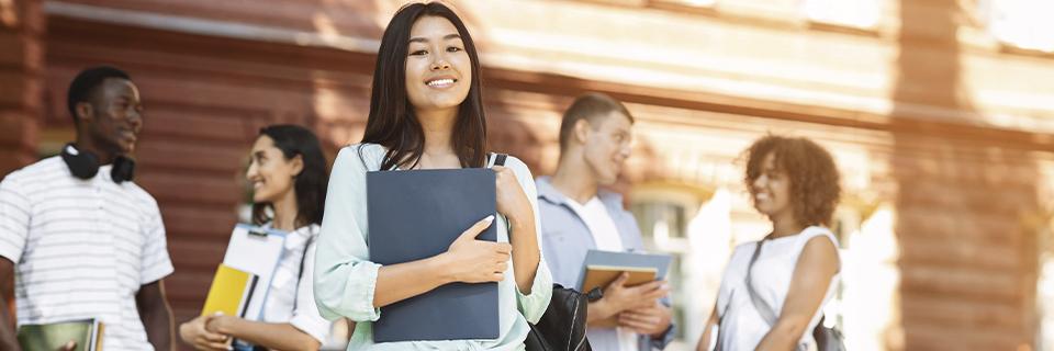 A confident international student holding books and smiling on a U.S. campus, symbolizing young EB5 investors exploring Green Card options.