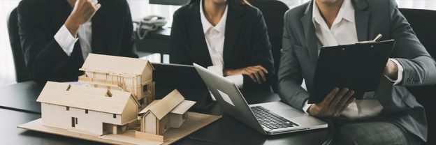 Three business professionals in suits reviewing a real estate model and financial documents in an office, symbolizing EB5 project planning and due diligence with third-party lenders.
