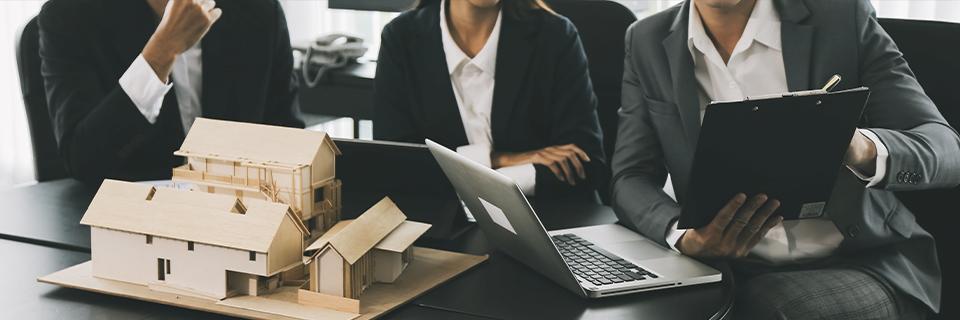 Three business professionals in suits reviewing a real estate model and financial documents in an office, symbolizing EB5 project planning and due diligence with third-party lenders.