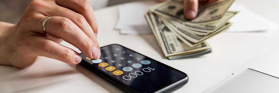 An investor calculating EB5 fund transfers on a smartphone with U.S. dollar bills in hand, illustrating flexible funding options for EB5 through phased payments.