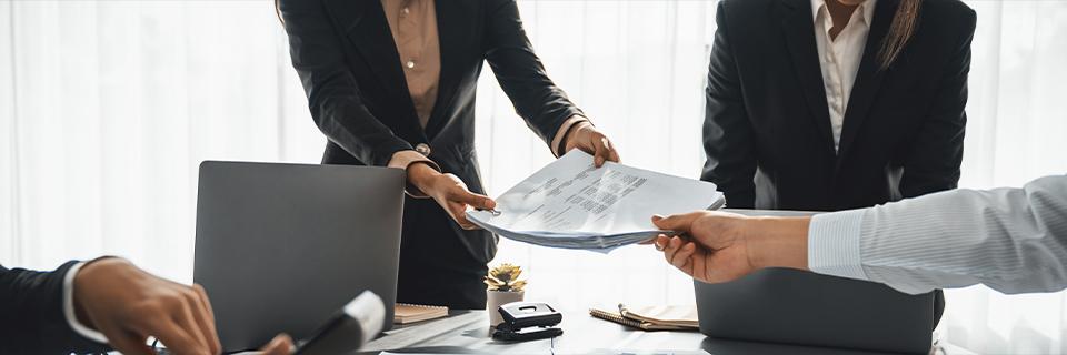 Business team exchanging financial documents across a conference table, illustrating third-party oversight and monitoring in EB5 project development.