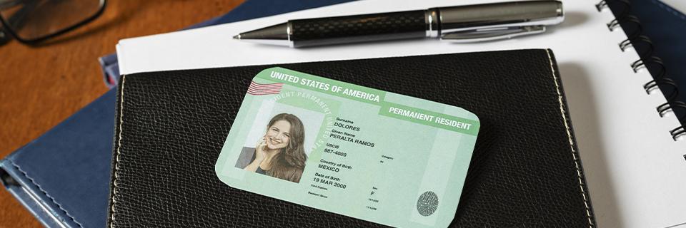 U.S. Permanent Resident Card placed on a black notebook with a pen, illustrating the benefits of EB5 Green Card ownership and legal residency.