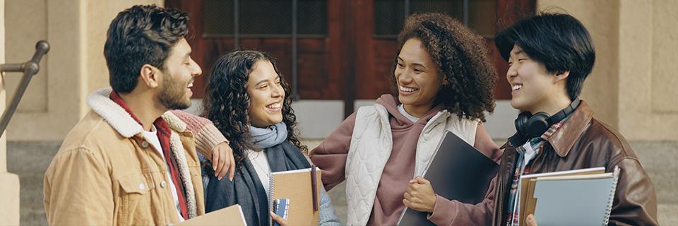 A diverse group of international students talking and laughing outside a university building, representing the growing interest in EB5 Green Cards among F1 visa holders.