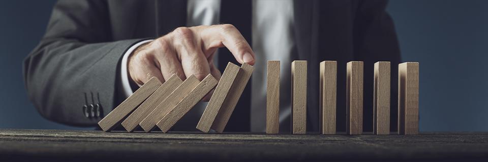 A businessman in a suit stopping a row of falling wooden dominoes, symbolizing EB5 investors managing financial risk under the at-risk requirement.