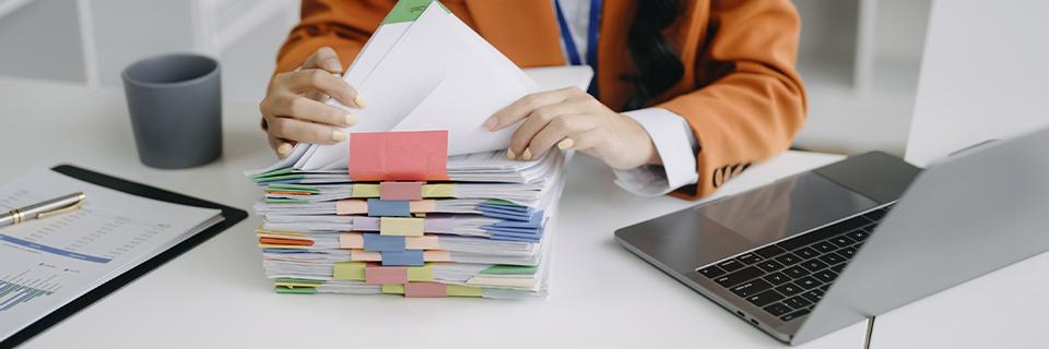 Hands sorting stacks of immigration case files with colored tabs beside a laptop, symbolizing EB5 petition processing and documentation review.