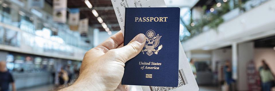 A hand holding a U.S. passport and boarding pass at an airport, symbolizing the travel freedom and global mobility that comes with U.S. citizenship.