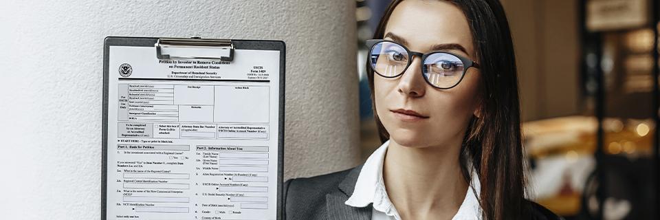 A professional woman holding a USCIS EB5 petition form on a clipboard, clarifying whether petition approval is a criterion in the end of the at-risk requirement.