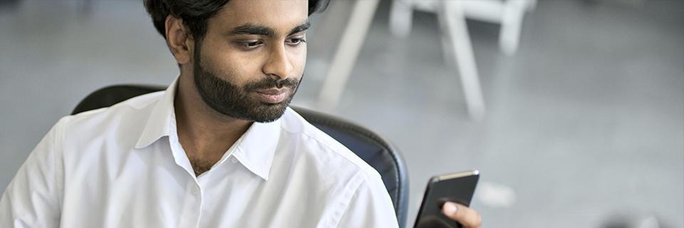 An Indian tech worker looking at his smartphone in an office, symbolizing H1B employees researching EB5 visa opportunities for U.S. permanent residency.