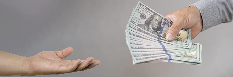 Close-up of one hand passing U.S. dollar bills to another, illustrating EB5 investment funds being deployed into a project to stay at risk.