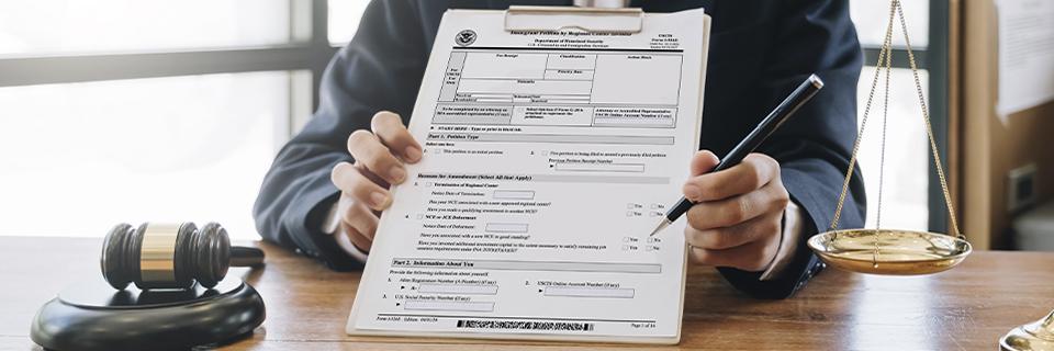An attorney holding a USCIS immigration form on a clipboard beside a gavel and justice scale, symbolizing EB5 mandamus litigation for delayed petitions.