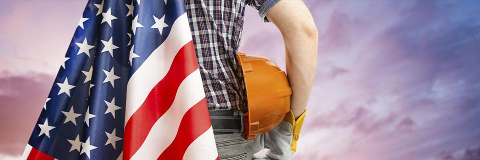 A construction worker draped in the American flag holding a hard hat, symbolizing EB5 investors creating jobs that strengthen U.S. industries and communities.