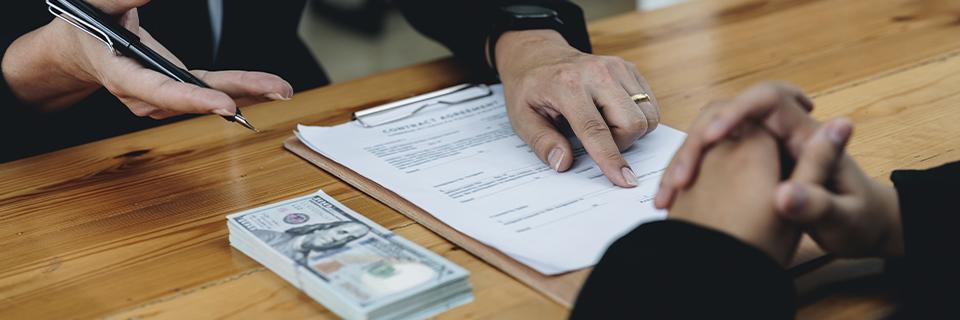 An investor reviewing a contract with cash on the table, symbolizing EB5 loan agreements and financial compliance risks.