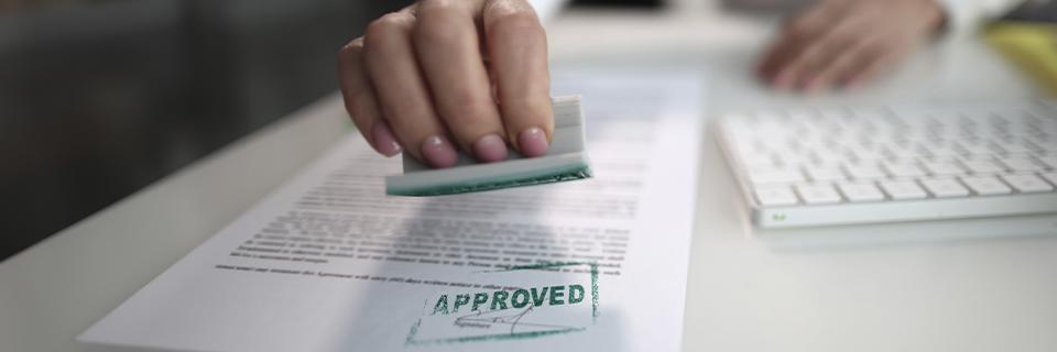 Close-up of a hand stamping “Approved” on official paperwork, symbolizing EB5 petition approval and successful resolution after delays.