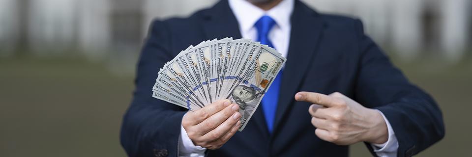 A businessman holding a fan of hundred-dollar bills, illustrating the risks of using loans from regional centers for EB5 investment capital.