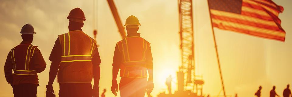 Three construction workers in safety vests walking at sunset with the American flag in the background, symbolizing EB5 job creation and U.S. economic growth.
