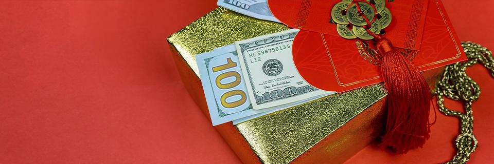 Hundred-dollar bills placed on a decorated gift box with red envelopes, illustrating EB5 investment funds received through gifts or inheritance.