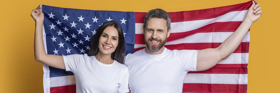 A smiling couple holding up the American flag, representing EB5 investors achieving conditional permanent residency and beginning their path to U.S. citizenship.