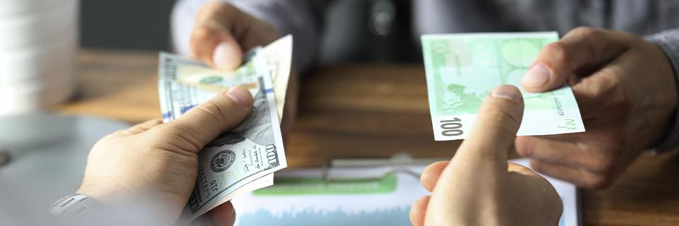 Hands exchanging U.S. dollars and euros across a desk, representing EB5 path of funds and international money transfers for investment.