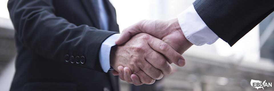 Close-up of two businessmen shaking hands outdoors in front of office buildings, symbolizing EB5 trust, agreements, and successful partnerships.