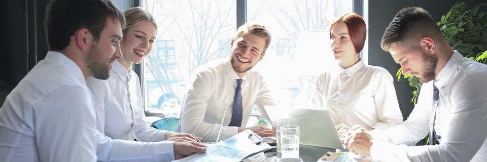 A group of professionals collaborating around a laptop in a bright office, representing EB5 investor support, due diligence, and advisory services.
