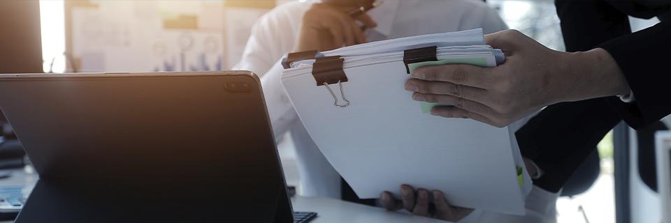 Business professionals reviewing clipped financial documents beside a laptop, showing EB5 path of funds documentation and record-keeping.