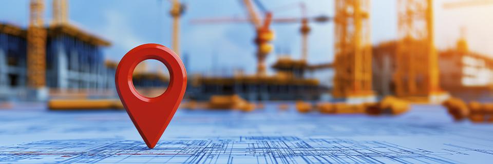 Red location marker on construction blueprints with cranes in the background, reflecting EB5 project development and job creation in targeted employment areas.