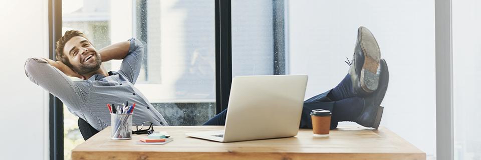 Relaxed businessman leaning back at his desk with laptop and coffee, symbolizing the ease and freedom of a passive EB5 investment managed by a regional center.