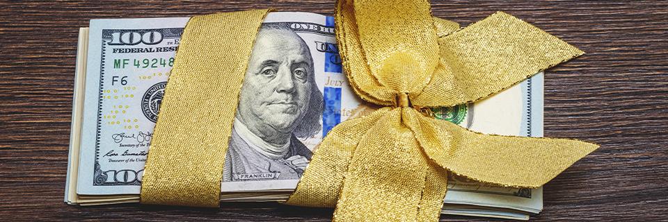 Stack of hundred-dollar bills tied with a gold ribbon, symbolizing gifted EB5 investment funds lawfully transferred from relatives to meet program requirements.