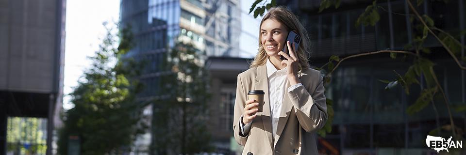 Confident young woman walking in a modern city with coffee and phone, reflecting EB5 investors enjoying mobility and flexibility while their regional center investment works toward Green Card goals.