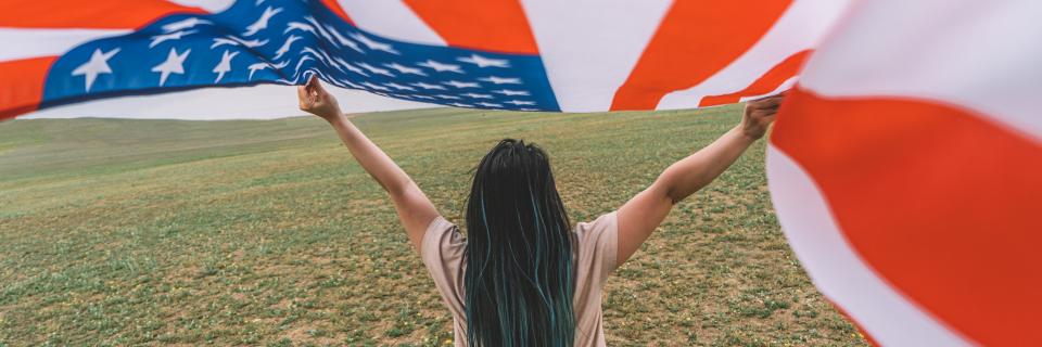 A person holding a large U.S. flag in an open field, expressing the goal of securing permanent residency through the EB5 program.