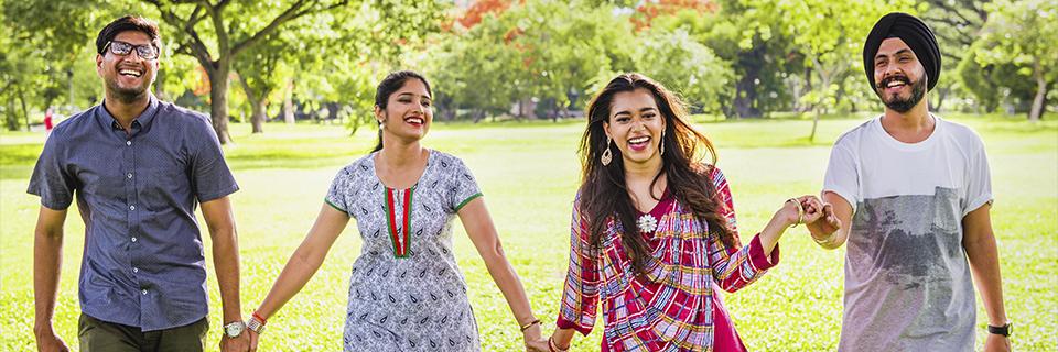 Group of young Indian professionals smiling and walking together in a park, reflecting how EB5 offers Indian H-1B holders a secure path to permanent residency in the United States.