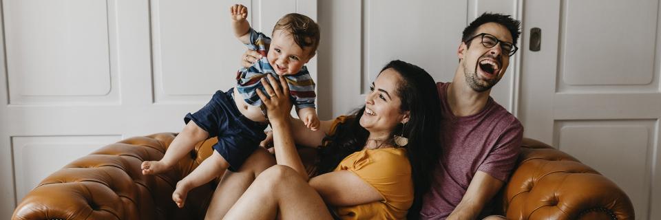 Smiling family with parents and a baby relaxing at home, illustrating how EB5 investment supports long-term family security, residency, and future opportunities in the United States.