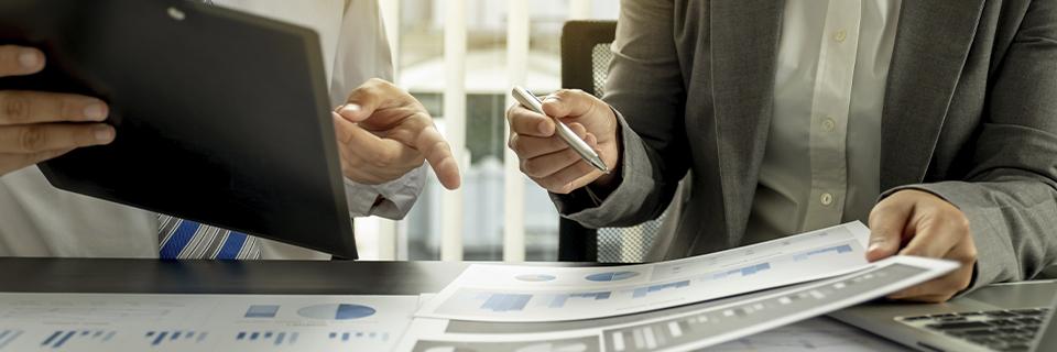 Business professionals reviewing financial charts on a laptop and printed reports, reflecting transparent EB5 project reporting and investor oversight.