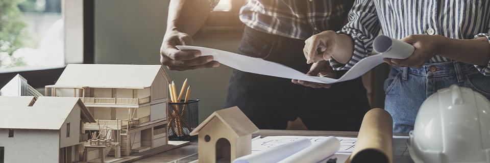 Developers reviewing architectural plans beside scale building models and construction tools, representing EB5 real estate projects, capital stack planning, and sustainable job-creating developments.